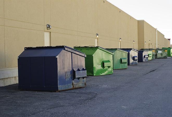 a construction worker unloading debris into a blue dumpster in Andover